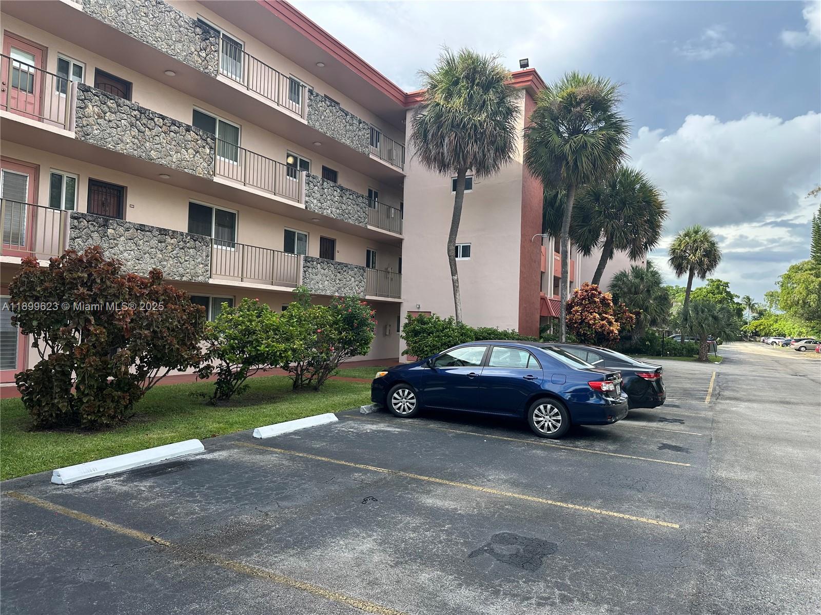 A multi-story apartment building with stone accents and balconies sits beside a parking lot — 1101 NW 58th Ter # 108, Sunrise FL 33313, SUNRISE, FL