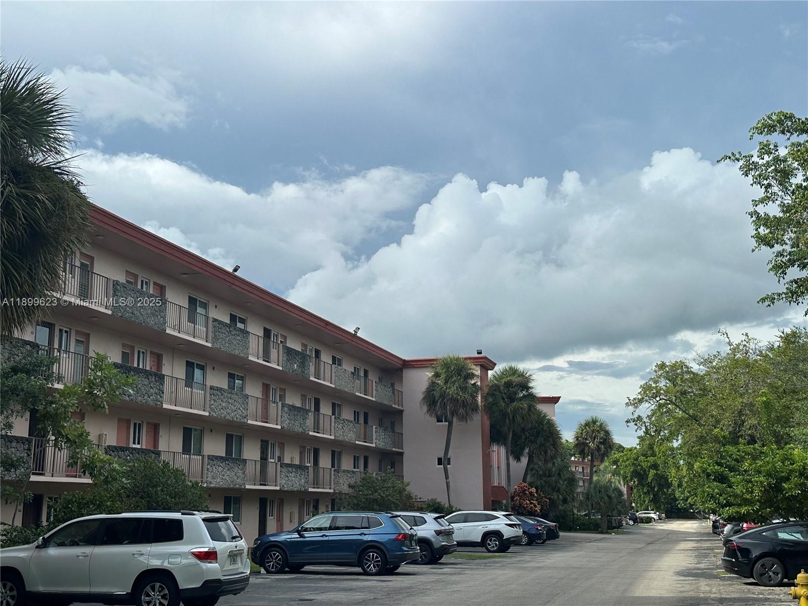 A multi-story apartment building with balconies stands next to a parking lot with several cars — 1101 NW 58th Ter # 108, Sunrise FL 33313, SUNRISE, FL