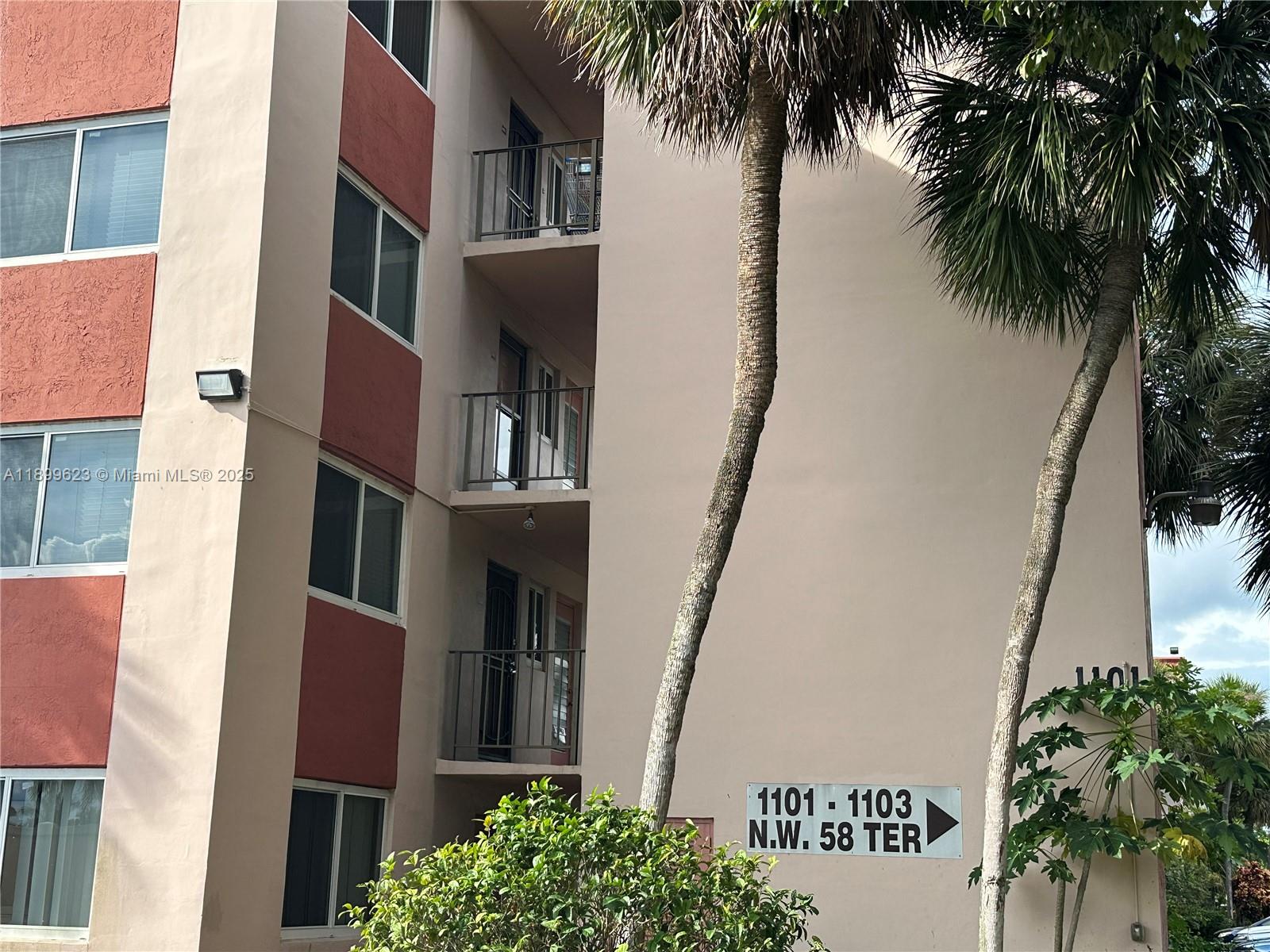 The exterior of a multi-story apartment building features balconies and a directional sign — 1101 NW 58th Ter # 108, Sunrise FL 33313, SUNRISE, FL