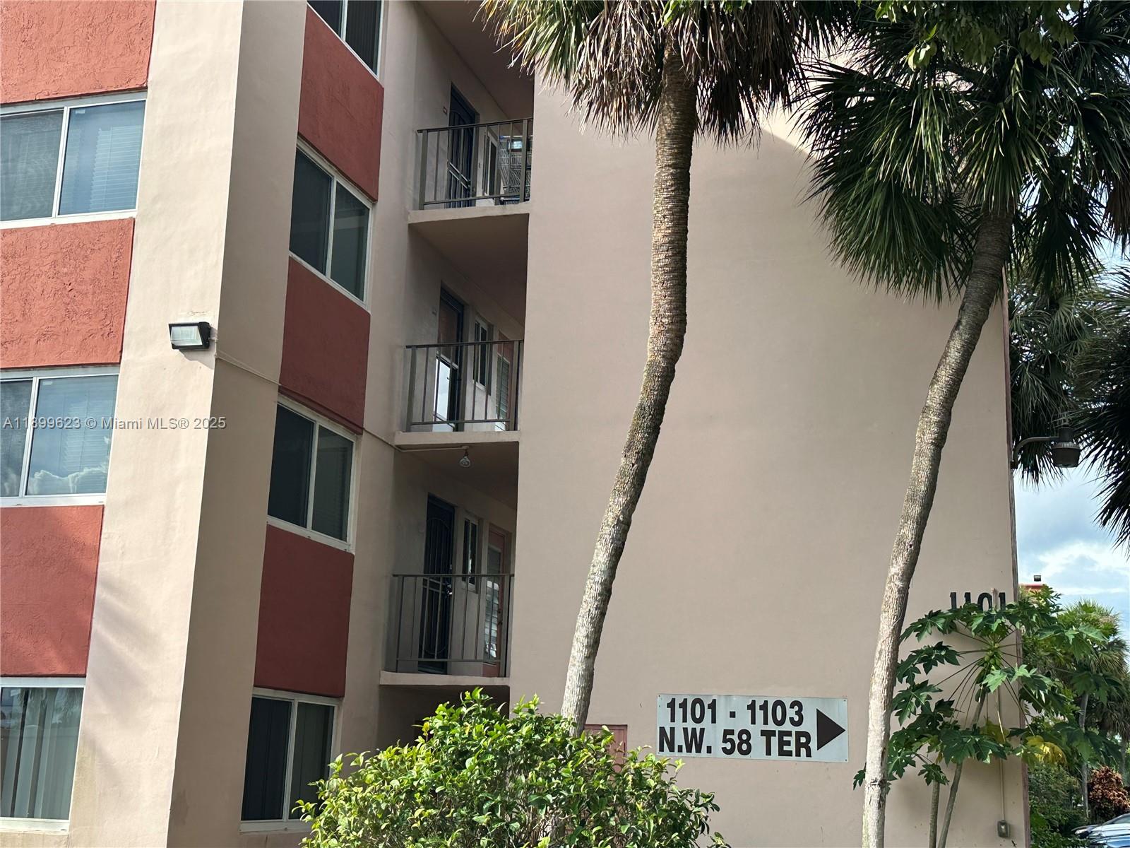 The exterior of a multi-story apartment building features balconies and a directional sign — 1101 NW 58th Ter # 108, Sunrise FL 33313, SUNRISE, FL