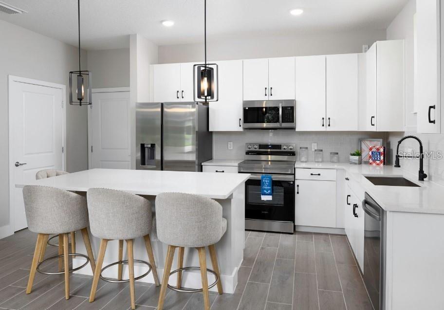 A modern kitchen features white cabinets, stainless steel appliances, a center island, and gray flooring — 2109 BROOME STREET, KISSIMMEE, FL