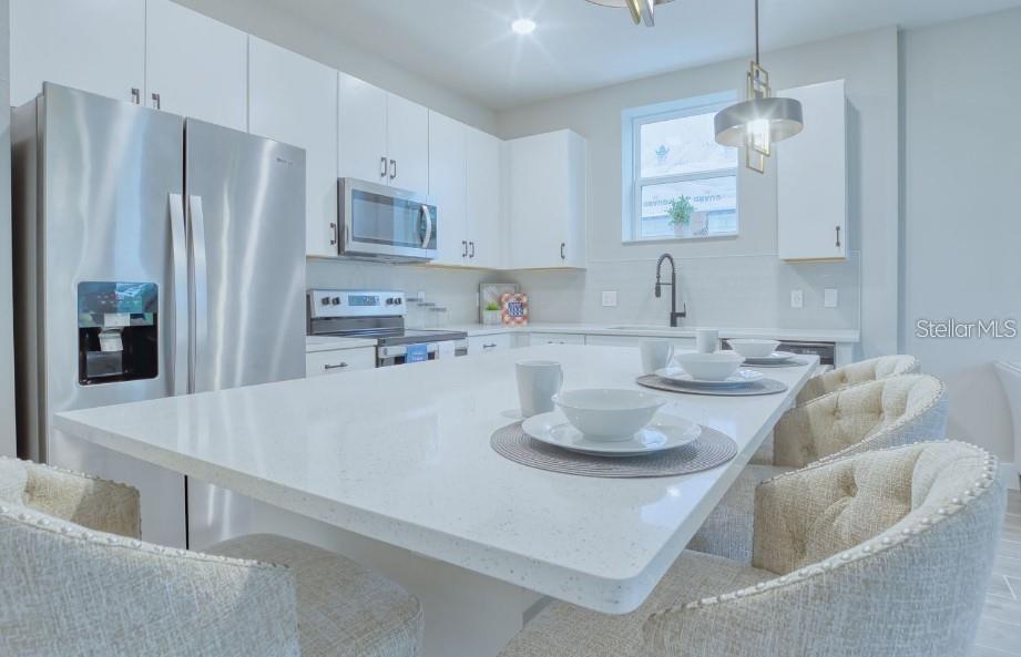 A modern kitchen features white cabinetry, stainless steel appliances, and a large quartz-topped island — 2109 BROOME STREET, KISSIMMEE, FL