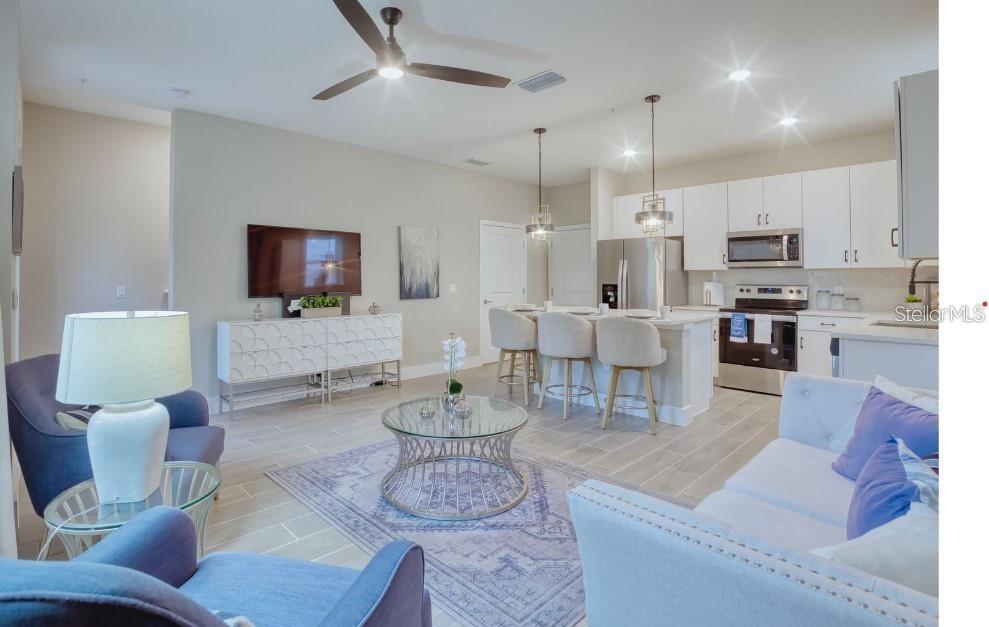 An open-concept living room and kitchen featuring white cabinetry, stainless steel appliances, and tile flooring — 2109 BROOME STREET, KISSIMMEE, FL