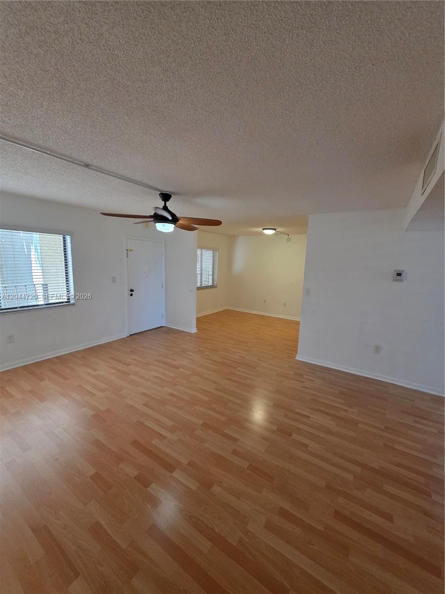 An empty living room features light wood-look flooring, white walls, and a ceiling fan — 8065 SW 107th Ave # 214, Miami FL 33173, MIAMI, FL