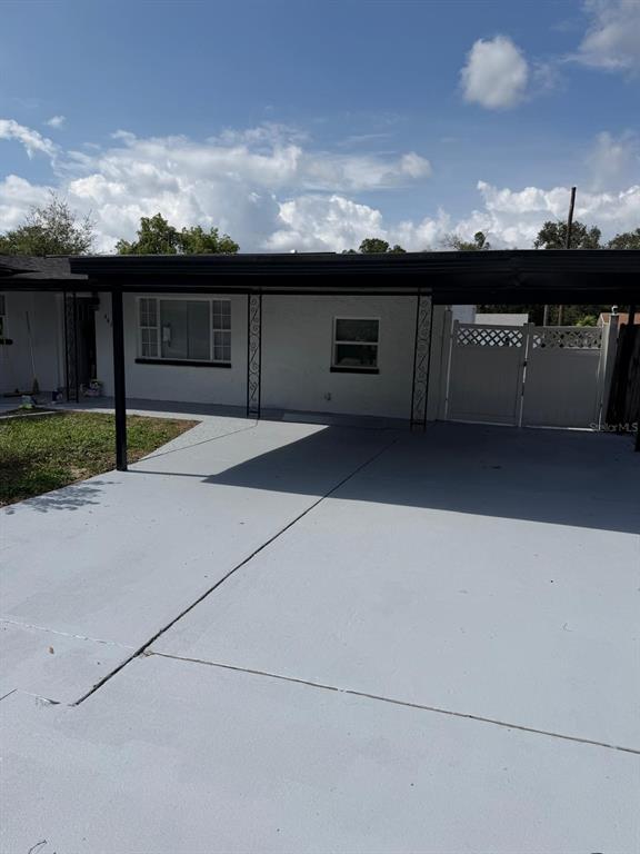 A white house exterior features a large gray concrete carport and a white privacy gate — 4416 COBIA DRIVE, TAMPA, FL