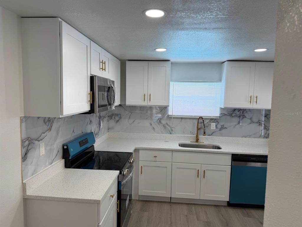 A kitchen with white cabinets, marble-patterned backsplash, quartz countertops, and stainless steel appliances — 4416 COBIA DRIVE, TAMPA, FL