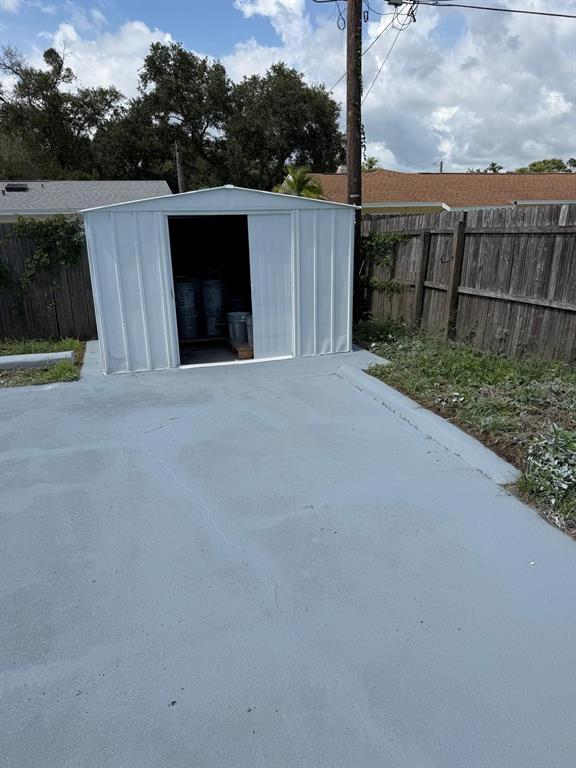 A white metal storage shed sits on a gray concrete pad in a fenced backyard — 4416 COBIA DRIVE, TAMPA, FL