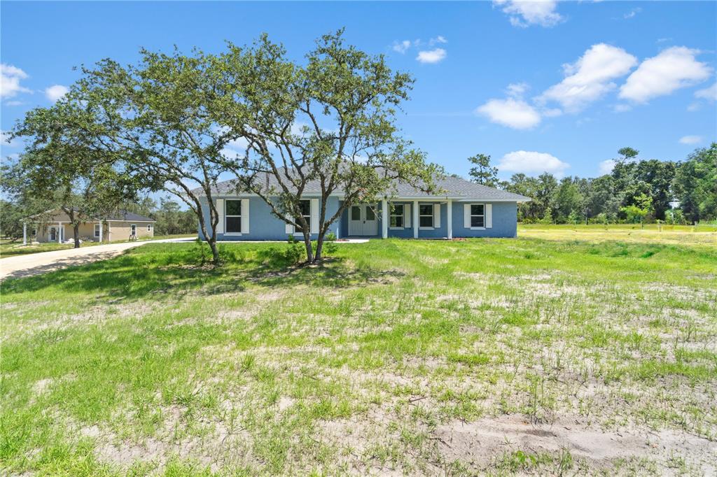 A blue single-story house with a gray roof sits on a large, grassy lot — 11751 NE 108TH STREET, ARCHER, FL