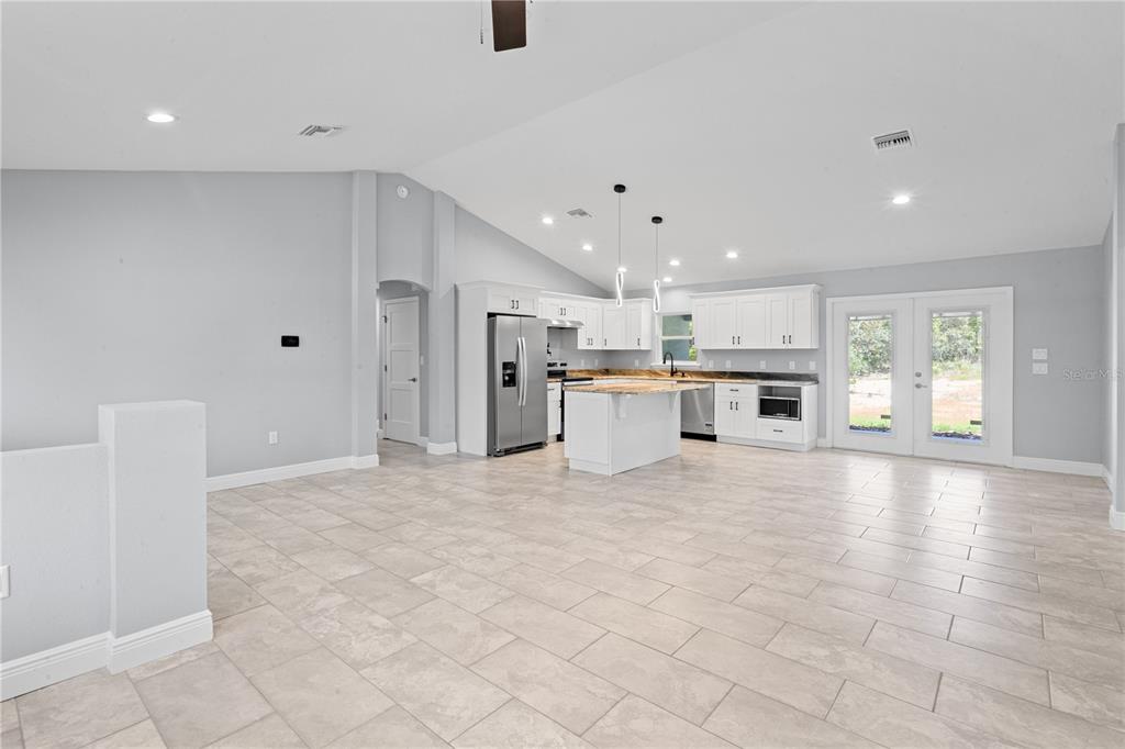A bright open-concept kitchen and living area features white cabinetry, a center island, and tile — 11751 NE 108TH STREET, ARCHER, FL