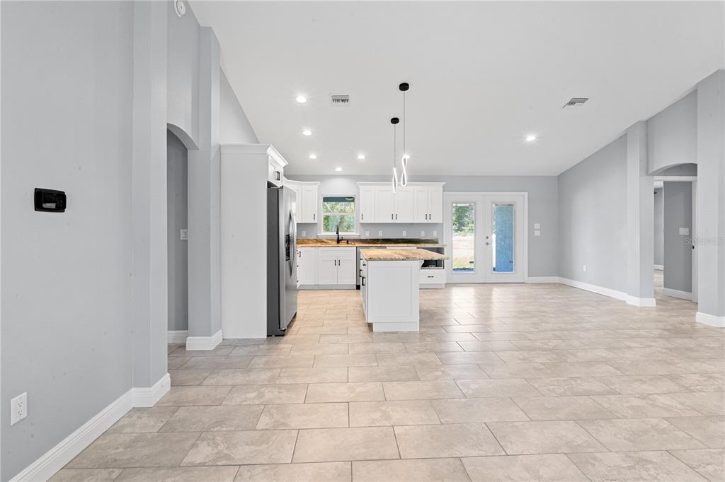 A bright, open-concept kitchen features white cabinetry, a central island, and light-colored tile flooring — 11751 NE 108TH STREET, ARCHER, FL