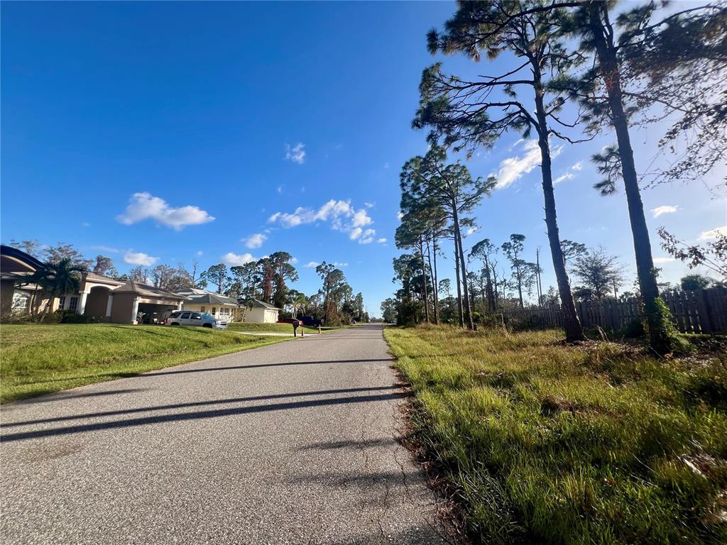 A paved residential street lined with houses on the left and tall pine trees — 5449 BURGNER STREET, PORT CHARLOTTE, FL