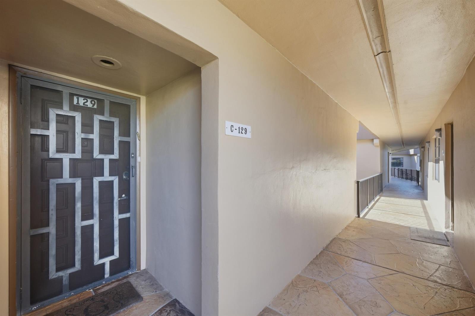 An outdoor apartment hallway features a brown door with a geometric metal security gate — 129 Piedmont C, Delray Beach FL 33484, DELRAY BEACH, FL