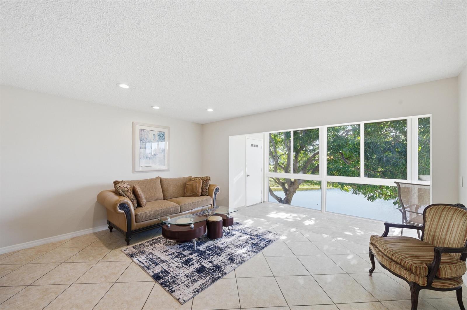 A living room with tile floors, a sofa, a coffee table, and large windows overlooking water — 129 Piedmont C, Delray Beach FL 33484, DELRAY BEACH, FL