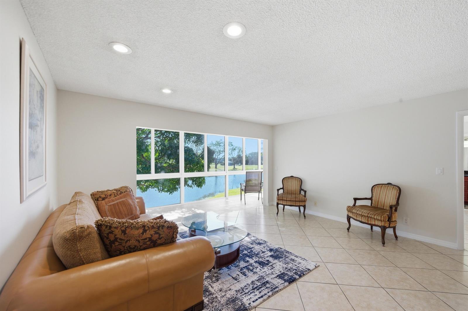 A living room features tile floors, a large window overlooking a lake, and three chairs — 129 Piedmont C, Delray Beach FL 33484, DELRAY BEACH, FL