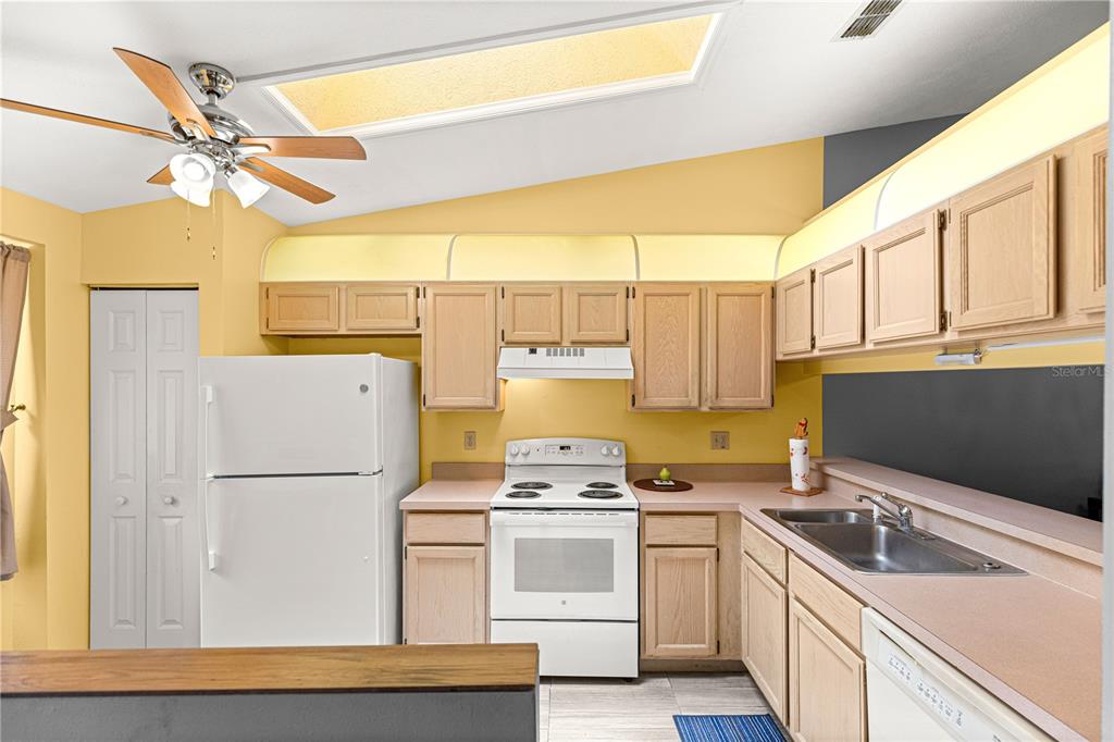 A kitchen with light wood cabinets, white appliances, yellow walls, and a skylight — 10483 SW 85TH COURT, OCALA, FL