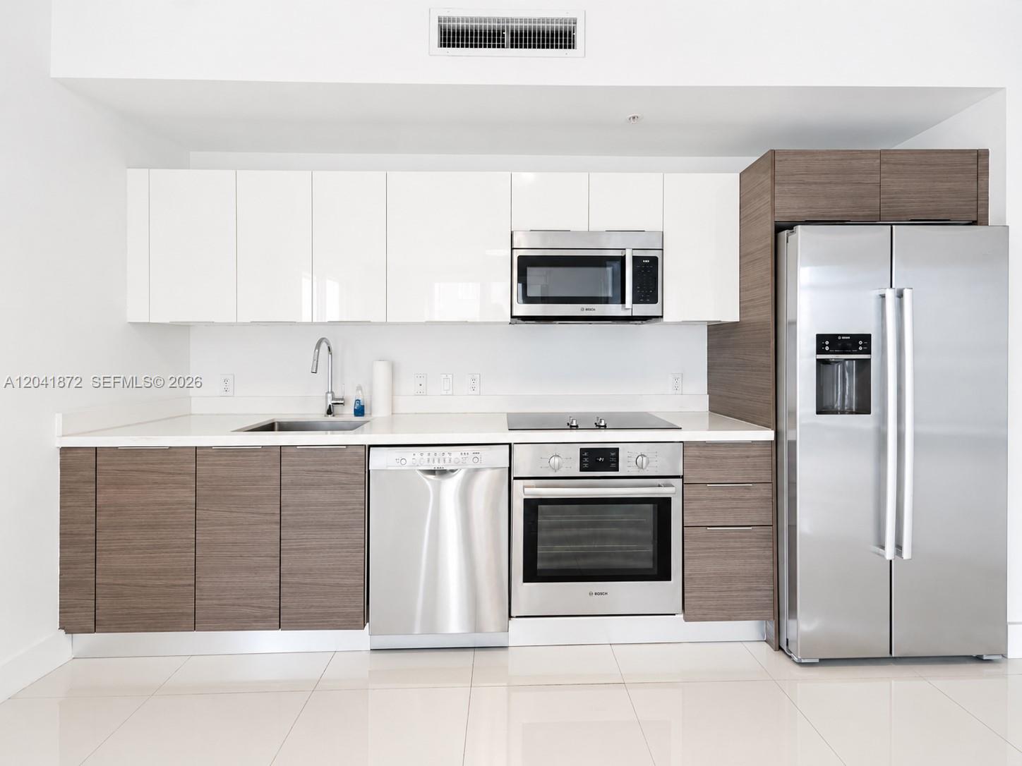 A modern kitchen features white upper cabinets, wood-tone lower cabinets, and stainless steel appliances — 1010 SW 2nd Ave # 1504, Miami FL 33130, MIAMI, FL
