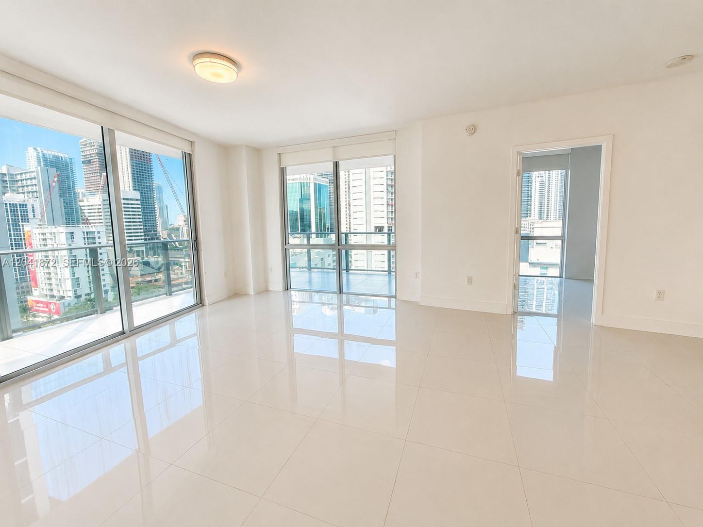 An empty room with white tile floors, large windows, and a doorway leading to another room — 1010 SW 2nd Ave # 1504, Miami FL 33130, MIAMI, FL