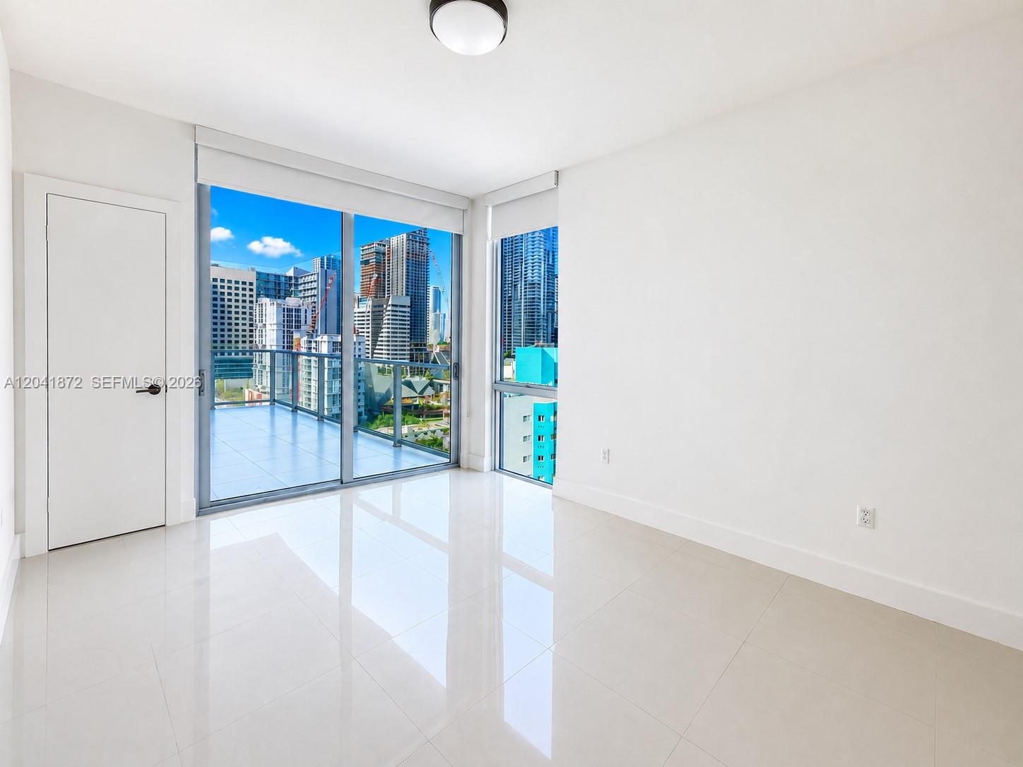 A bright, empty room features white walls, glossy tile floors, and a balcony with city views — 1010 SW 2nd Ave # 1504, Miami FL 33130, MIAMI, FL