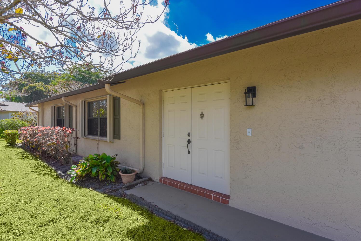 A beige house exterior features a double front door, a window, and a small garden — 1630 Palmland Drive, Boynton Beach FL 33436, BOYNTON BEACH, FL