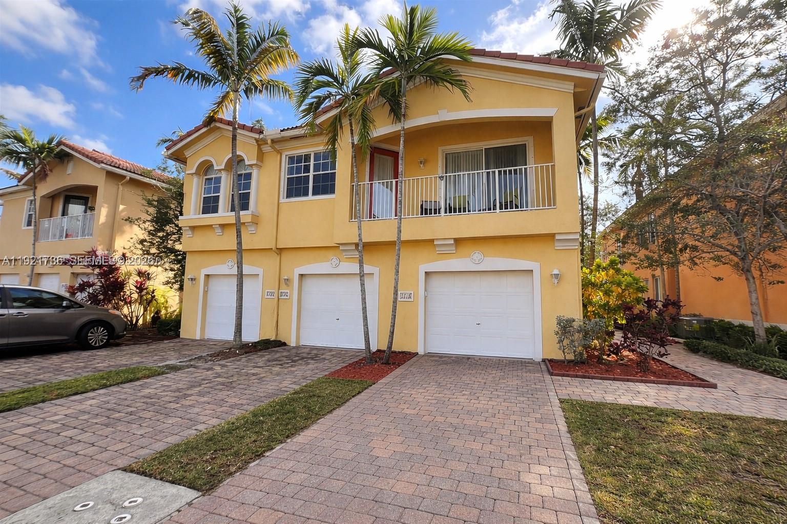A two-story yellow stucco townhouse features three garage doors and a second-floor balcony — 1718 Carvelle Dr # 1718, Riviera Beach FL 33404, RIVIERA BEACH, FL