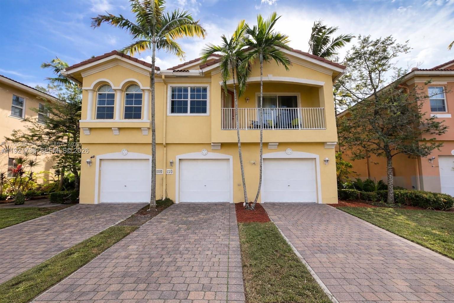 A yellow two-story townhouse features three garage doors and a second-floor balcony with palm trees — 1718 Carvelle Dr # 1718, Riviera Beach FL 33404, RIVIERA BEACH, FL