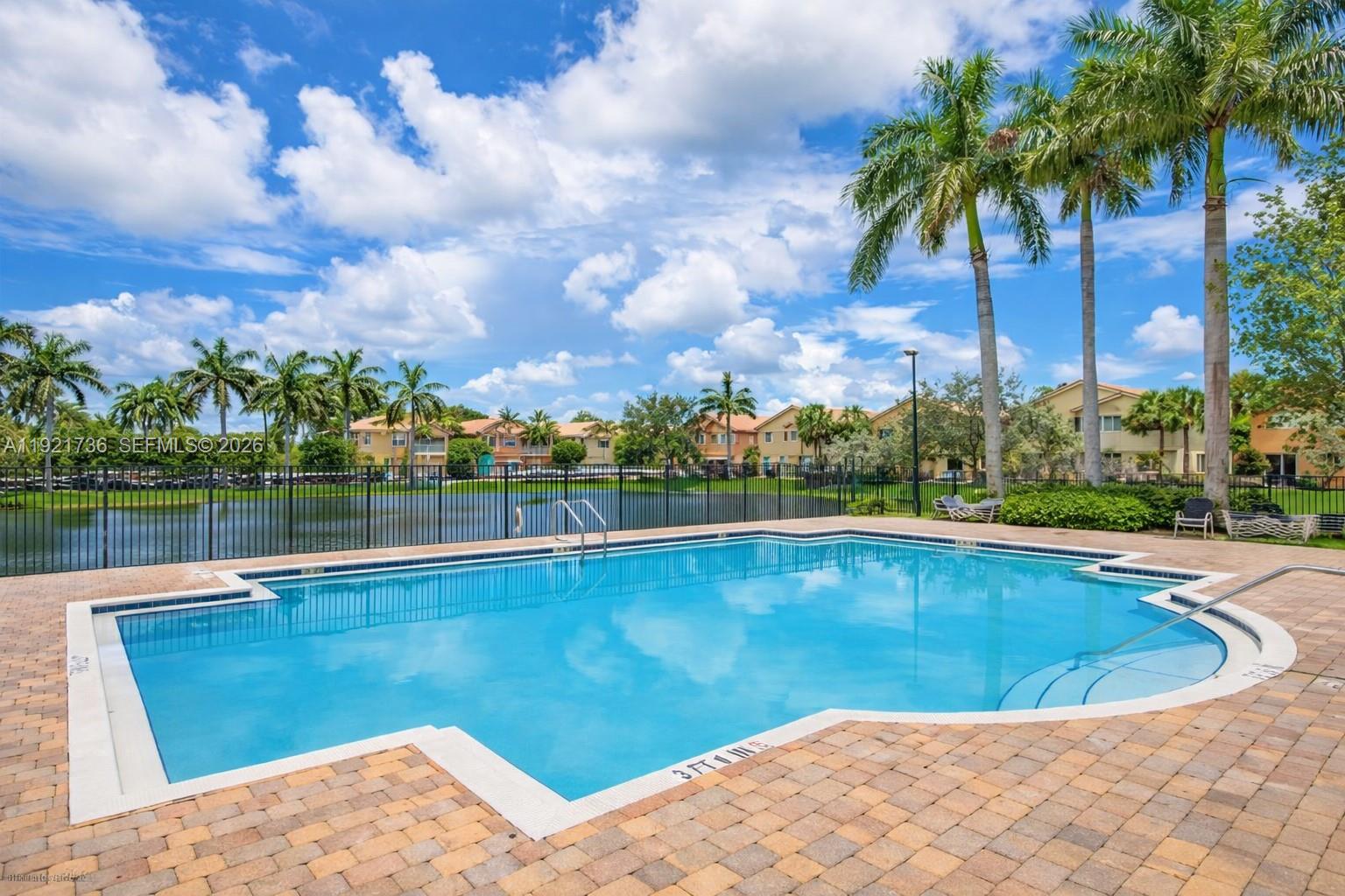 A swimming pool with a brick deck overlooks a lake and residential buildings — 1718 Carvelle Dr # 1718, Riviera Beach FL 33404, RIVIERA BEACH, FL