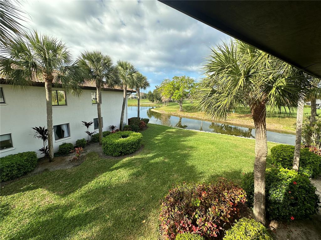 A view of a grassy lawn, palm trees, and a pond next to a building — 3500 EL CONQUISTADOR PARKWAY UNIT 344, BRADENTON, FL