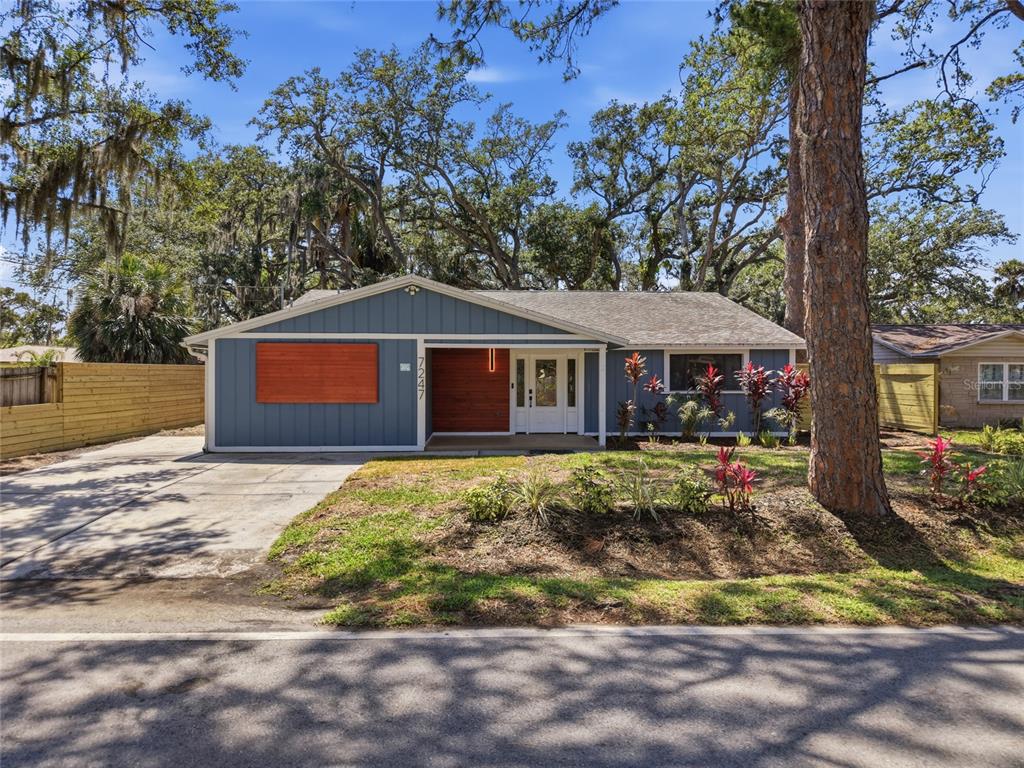 A single-story blue house with wood accents, a concrete driveway, and mature trees — 7247 OELSNER STREET, NEW PORT RICHEY, FL
