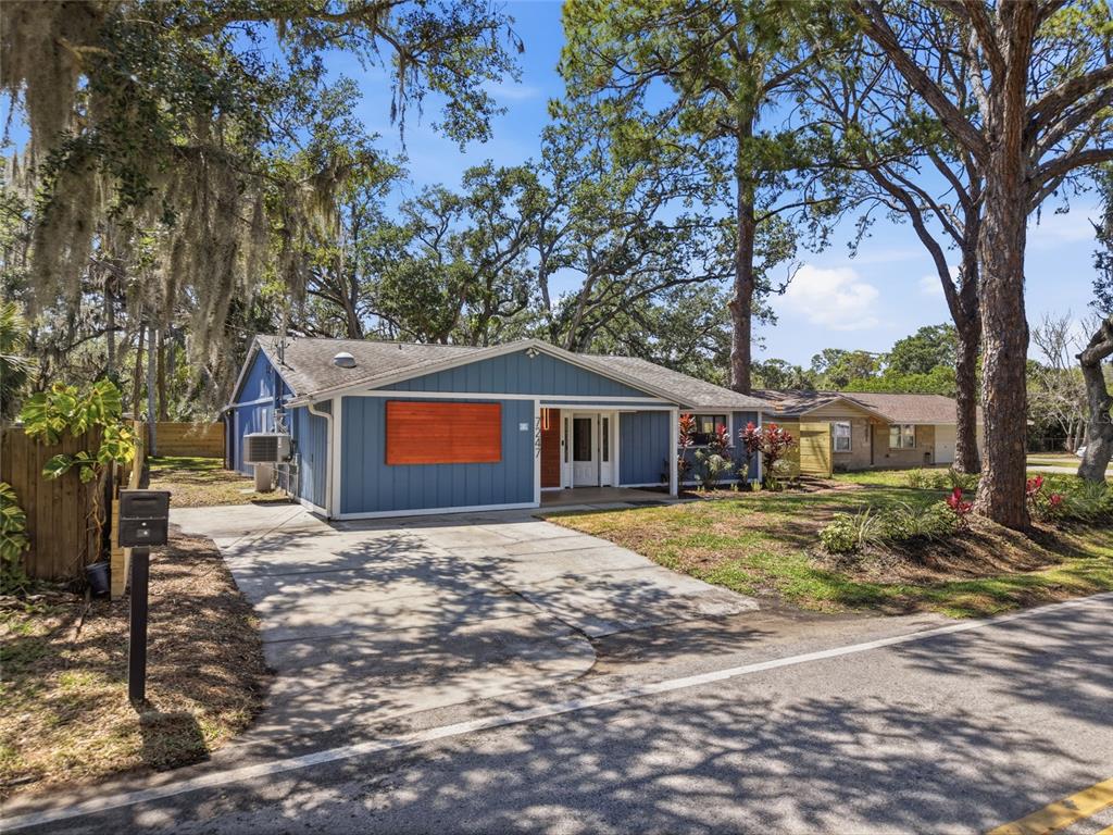 A blue single-story house with a concrete driveway and large trees in the front yard — 7247 OELSNER STREET, NEW PORT RICHEY, FL