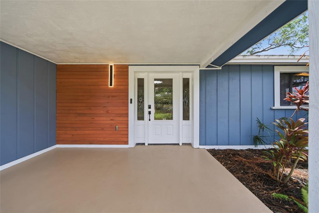 A covered entryway features a white front door, wood-paneled accent wall, and blue vertical siding — 7247 OELSNER STREET, NEW PORT RICHEY, FL