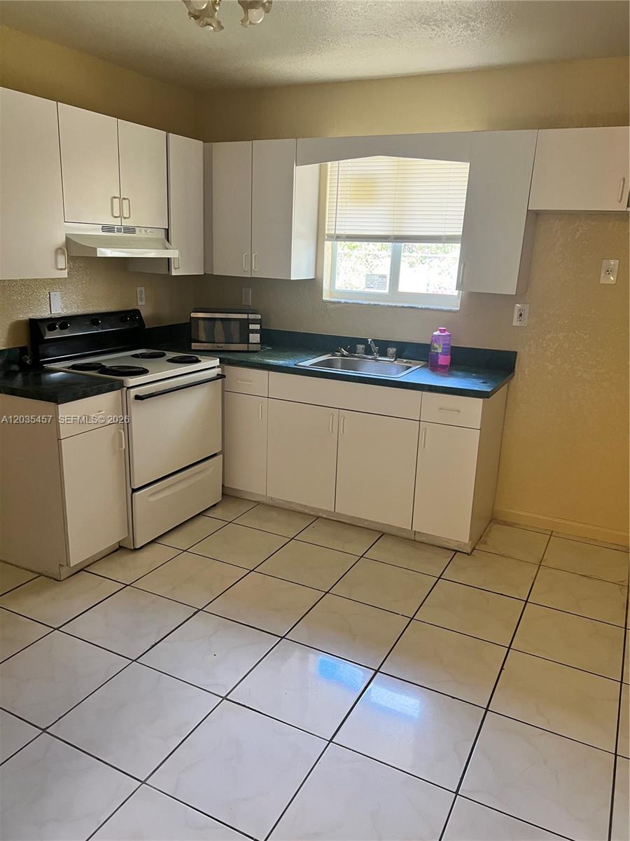 A kitchen features white cabinets, a white stove, a sink, and light-colored tiled flooring — 789 NW 55th Ter # B, Miami FL 33127, MIAMI, FL