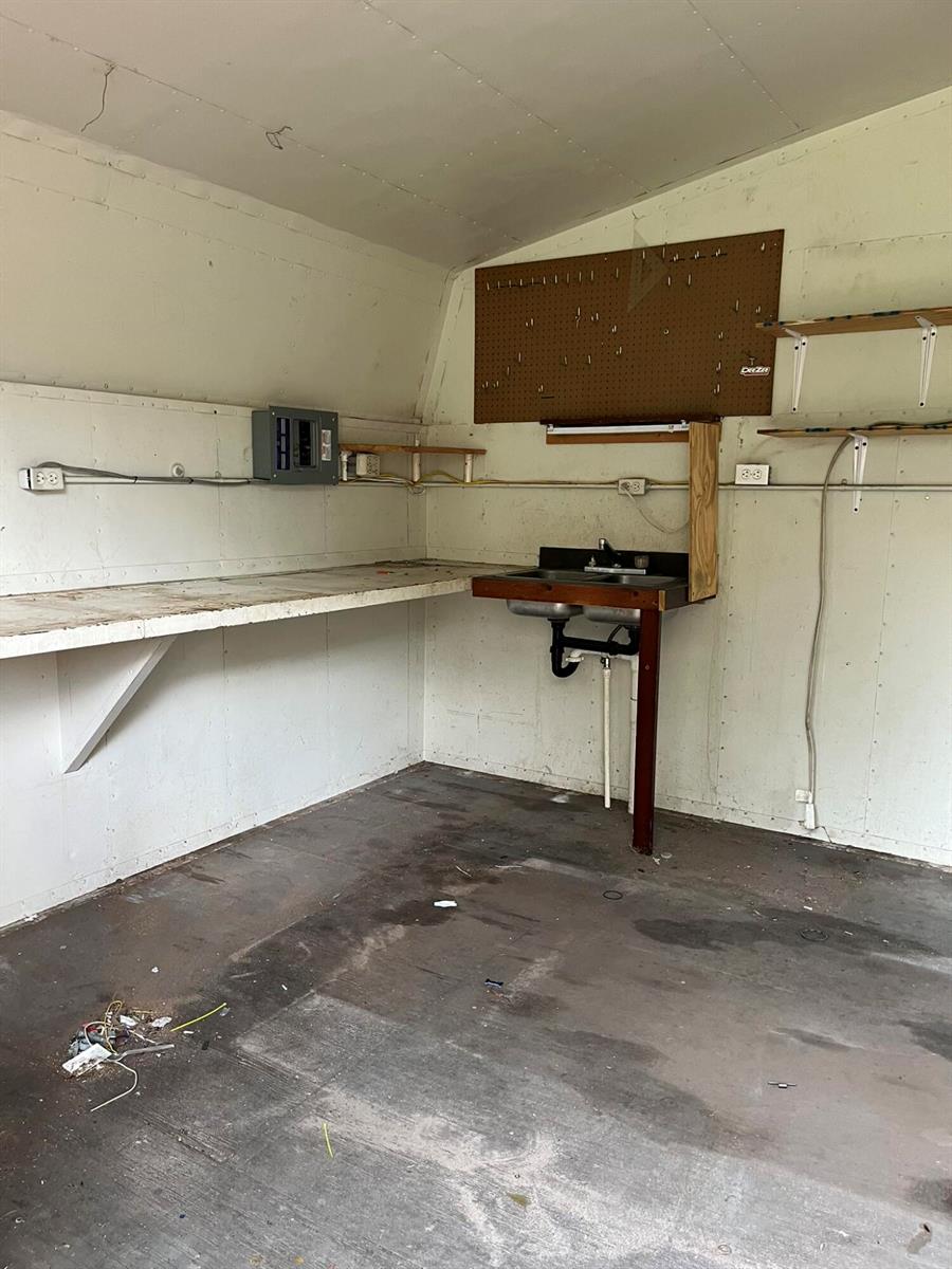 An unfinished shed interior features a workbench, a utility sink, pegboard, and exposed electrical wiring — 8956 SE 65th Way SE, Okeechobee FL 34974, OKEECHOBEE, FL