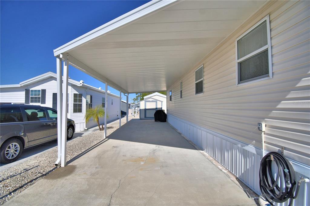 A concrete carport with a white metal roof extends alongside a light-colored mobile home — 251 PATTERSON ROAD UNIT B26, HAINES CITY, FL