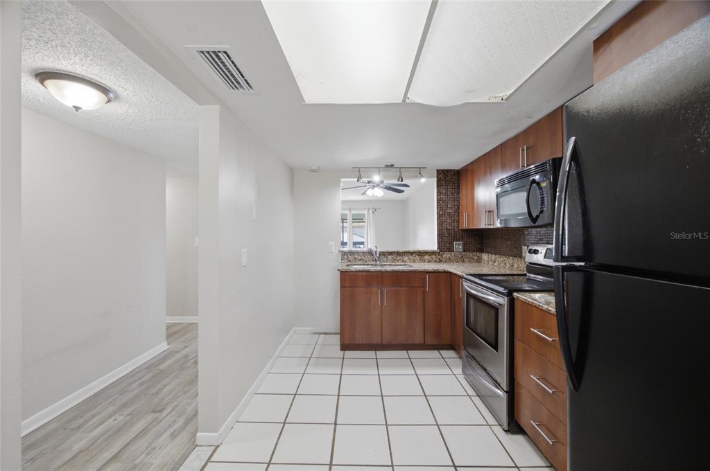 A kitchen features wood cabinets, stainless steel appliances, granite countertops, and white tile flooring — 6336 NEWTOWN CIRCLE UNIT 36C1, TAMPA, FL