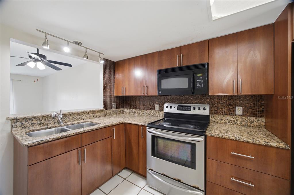A kitchen features wood cabinets, granite countertops, a stainless steel stove, and a tile backsplash — 6336 NEWTOWN CIRCLE UNIT 36C1, TAMPA, FL
