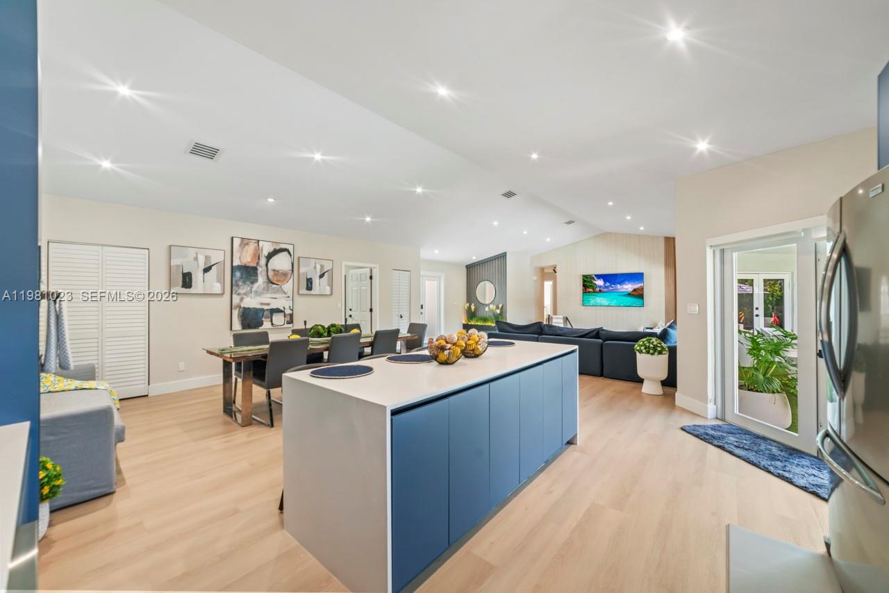 This open-concept kitchen and living area features a blue island, light wood flooring, and dining — 14481 SW 161st St, Miami FL 33177, MIAMI, FL