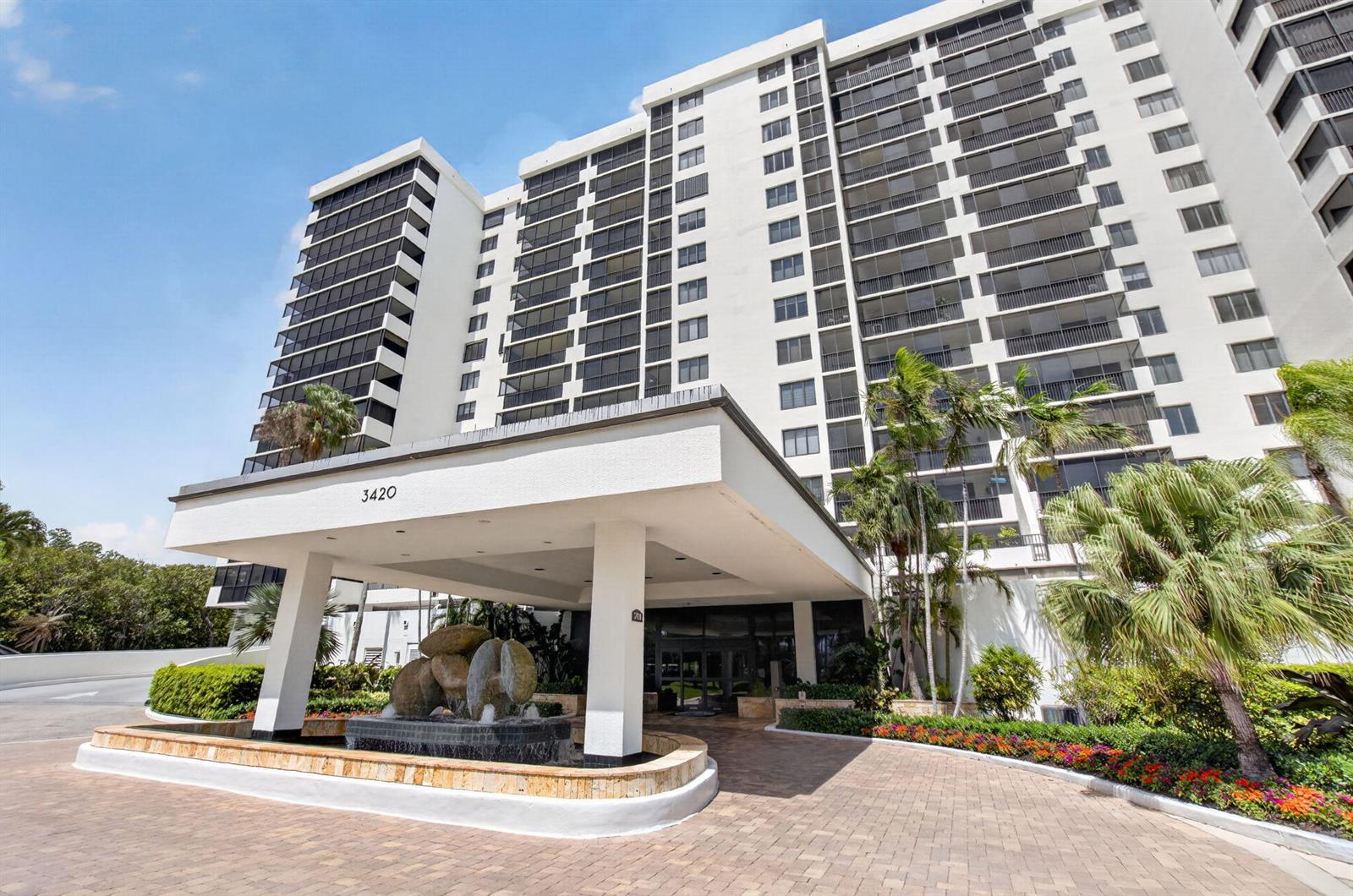 A multi-story white apartment building features a covered entrance with a stone fountain — 3420 S Ocean Boulevard # 12t, Highland Beach FL 33487, HIGHLAND BEACH, FL