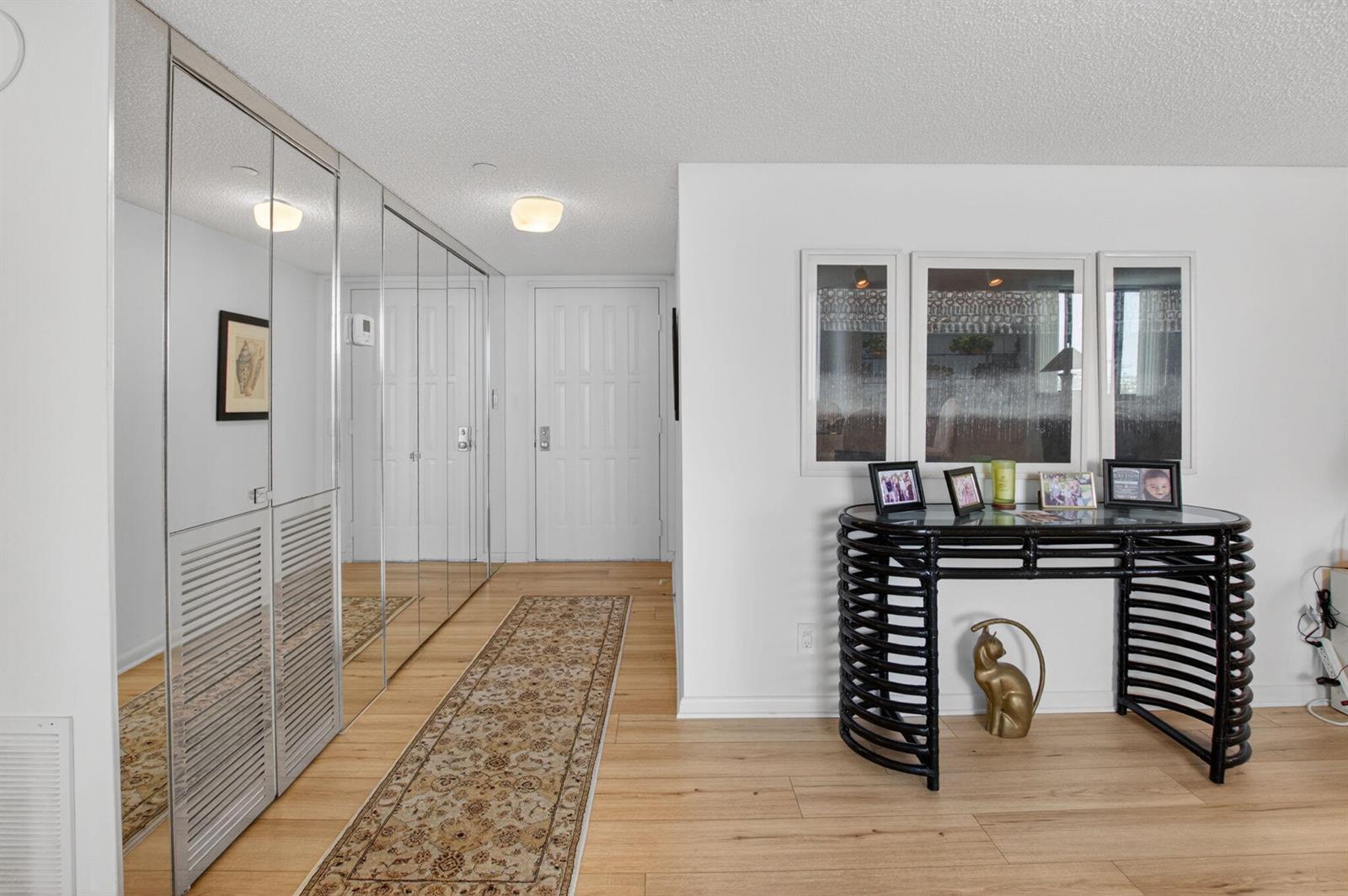 An entryway features light wood flooring, a runner rug, mirrored closet doors, and a console table — 3420 S Ocean Boulevard # 12t, Highland Beach FL 33487, HIGHLAND BEACH, FL