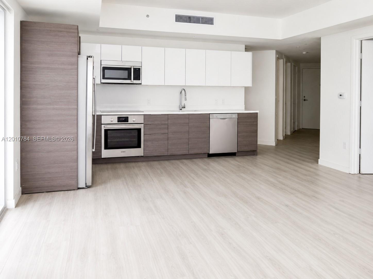 A modern kitchen features white upper cabinets, wood-tone lower cabinets, and stainless steel appliances — 1010 SW 2nd Ave # 1809, Miami FL 33130, MIAMI, FL