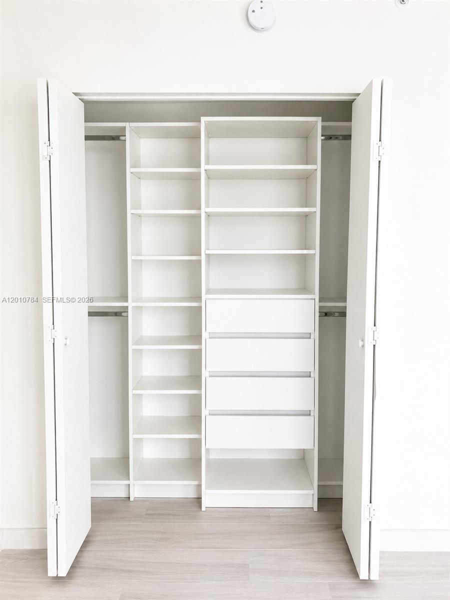A white reach-in closet features built-in shelving and four drawers against a light-colored wall — 1010 SW 2nd Ave # 1809, Miami FL 33130, MIAMI, FL