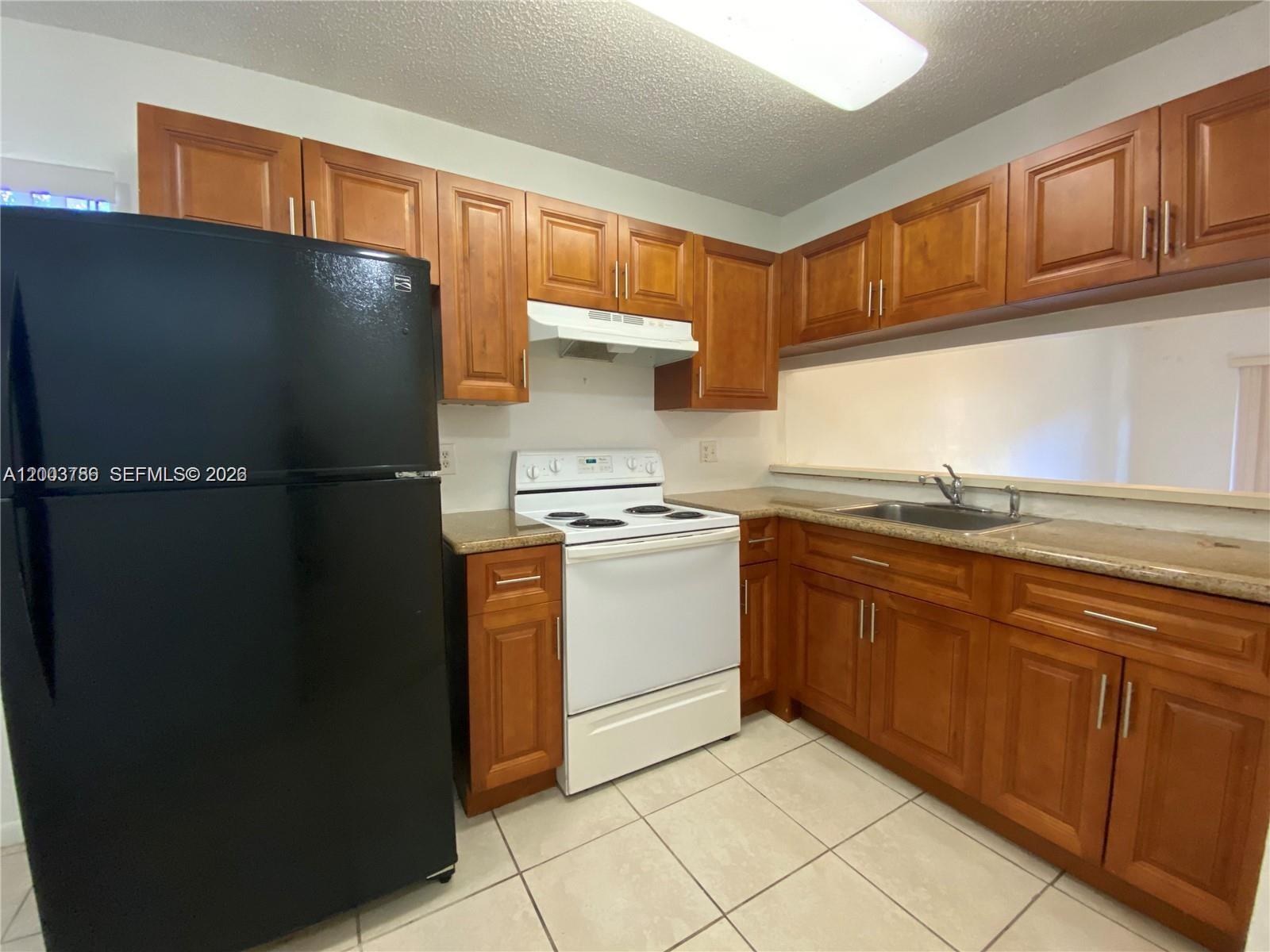 A kitchen features wood cabinets, a black refrigerator, a white stove, and tiled flooring — 4033 Lakeside Dr # 4033, Tamarac FL 33319, TAMARAC, FL