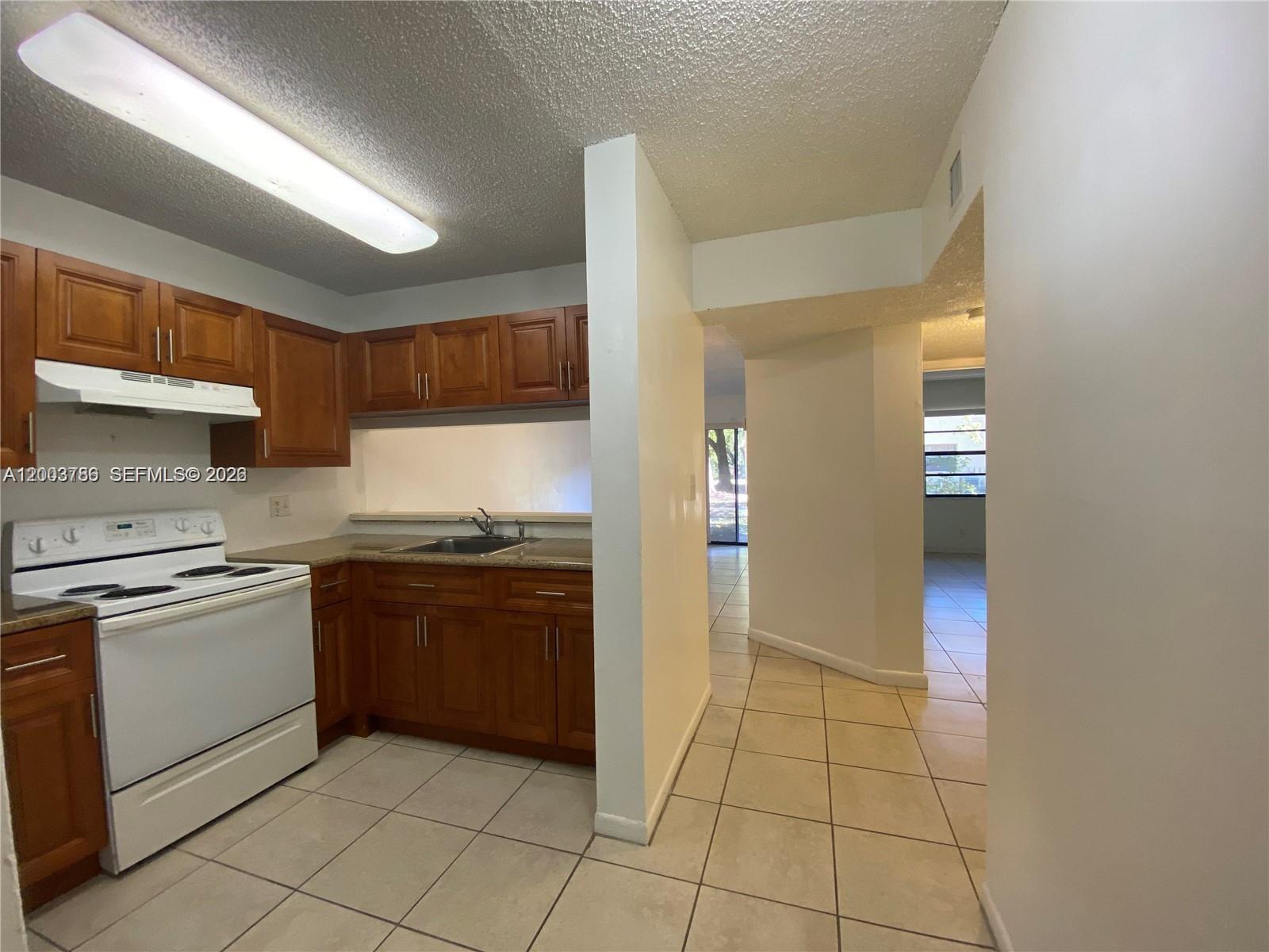 A kitchen with wood cabinets and white appliances opens to a tiled hallway and living area — 4033 Lakeside Dr # 4033, Tamarac FL 33319, TAMARAC, FL