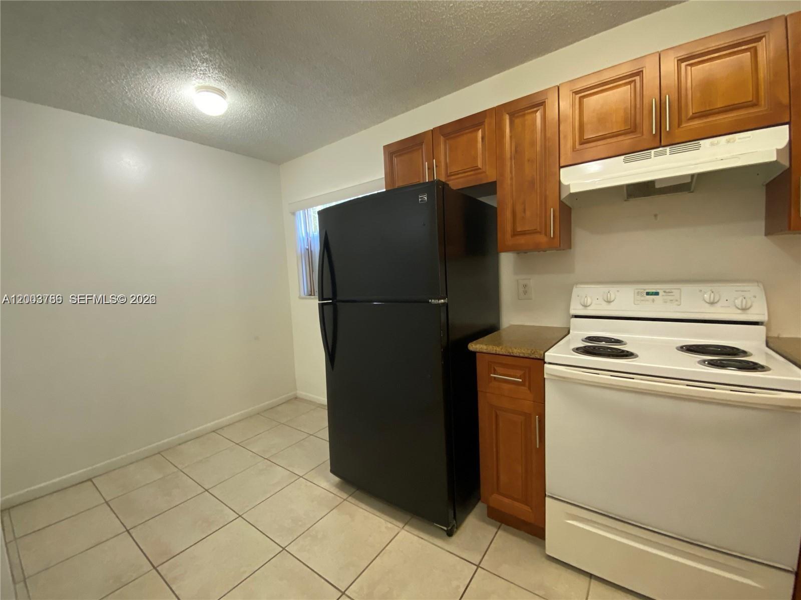 A kitchen features a black refrigerator, white stove, and wood cabinets over tiled flooring — 4033 Lakeside Dr # 4033, Tamarac FL 33319, TAMARAC, FL