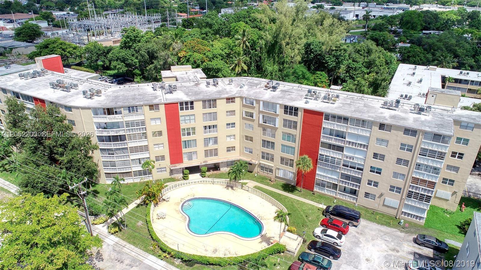 An aerial view of a multi-story apartment building with a swimming pool and parking lot — 1475 NE 125th Ter # 112A, North Miami FL 33161, NORTH MIAMI, FL