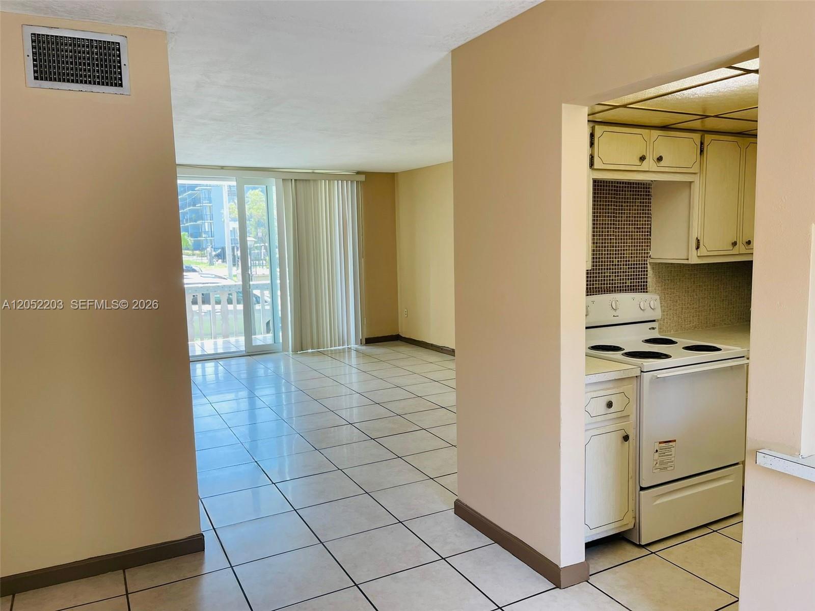A tiled living area leads to a balcony, with a kitchen visible on the right — 1475 NE 125th Ter # 112A, North Miami FL 33161, NORTH MIAMI, FL