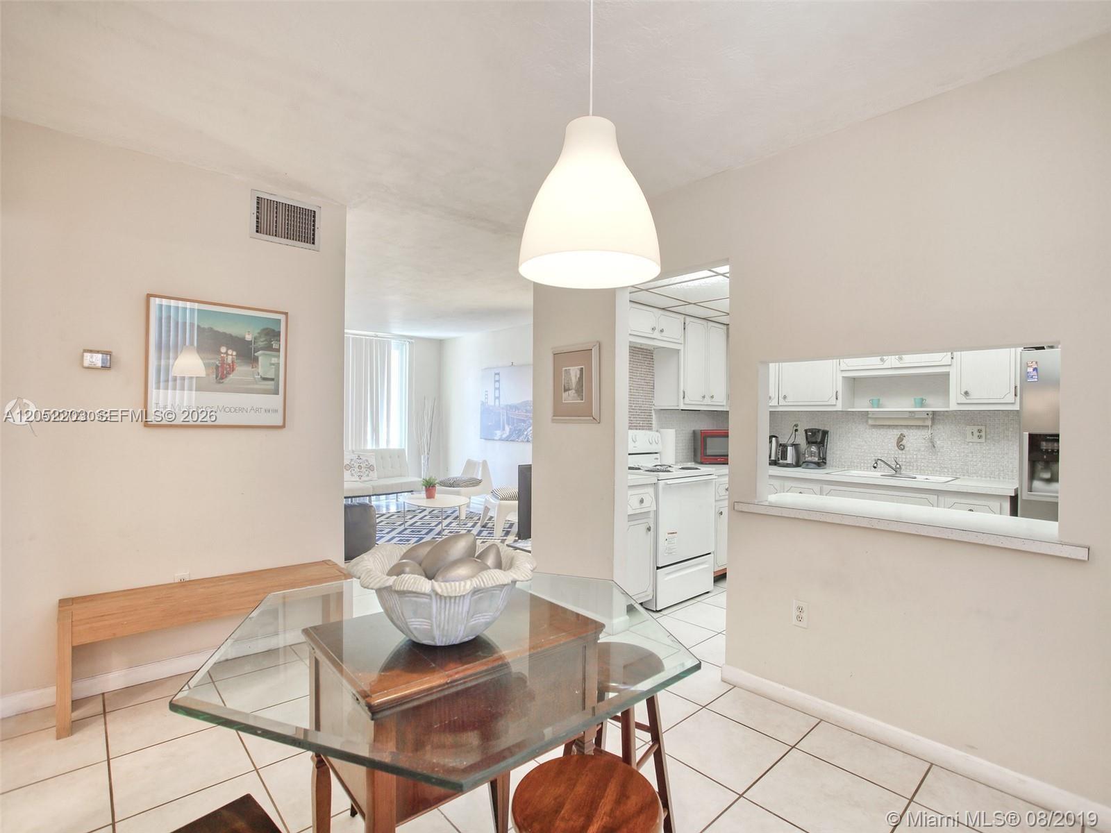 A dining area with a glass-topped table leads into a kitchen with white cabinetry — 1475 NE 125th Ter # 112A, North Miami FL 33161, NORTH MIAMI, FL