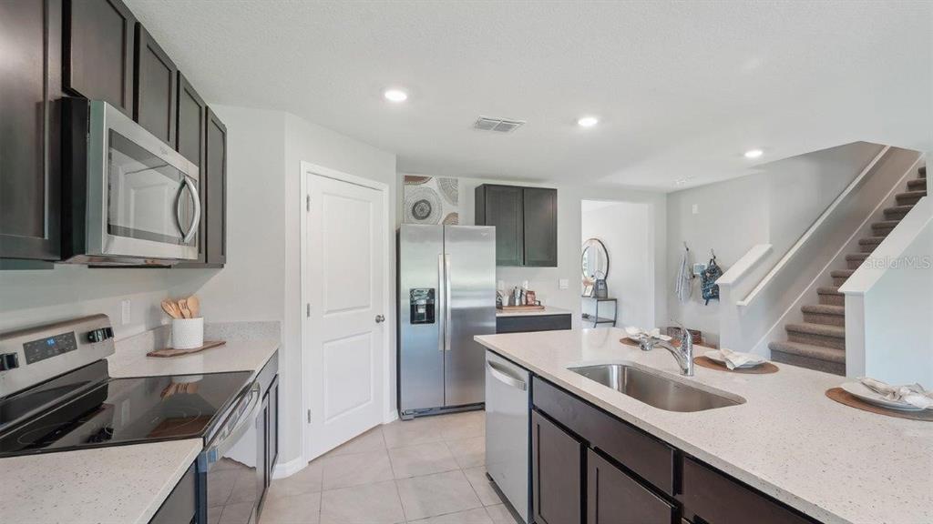 A modern kitchen features dark cabinets, stainless steel appliances, a kitchen island, and carpeted stairs — 35101 VALLEY RIDGE ROAD, DADE CITY, FL