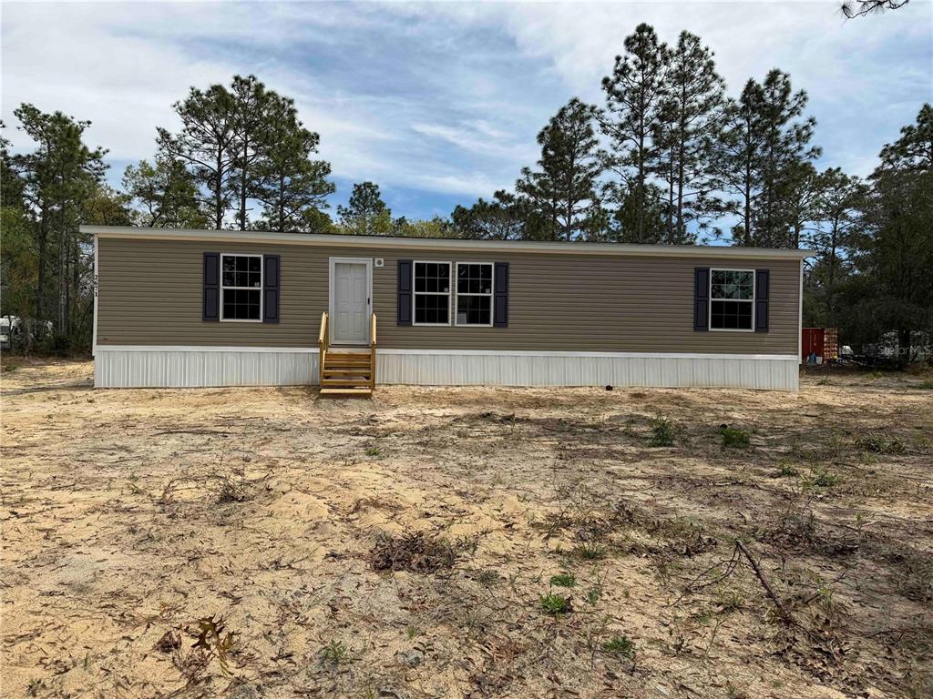A single-story manufactured home with tan siding and white skirting sits on a sandy lot — 2671 SE 133RD TERRACE, MORRISTON, FL