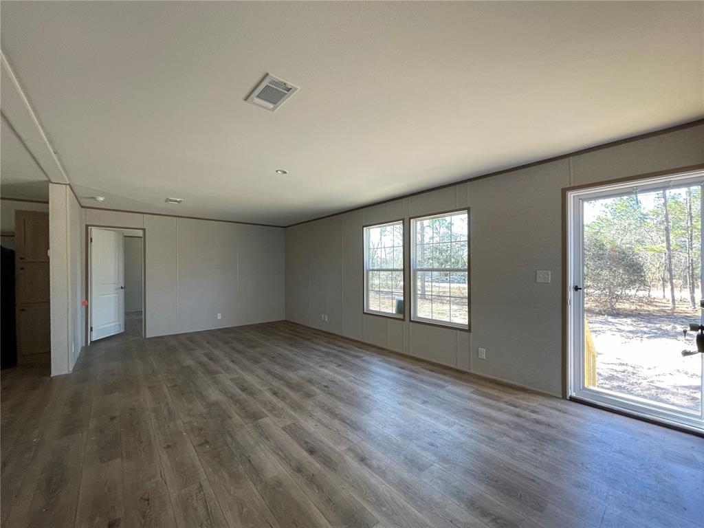 An empty room features light gray walls, wood-look flooring, two windows, and a sliding glass door — 2671 SE 133RD TERRACE, MORRISTON, FL
