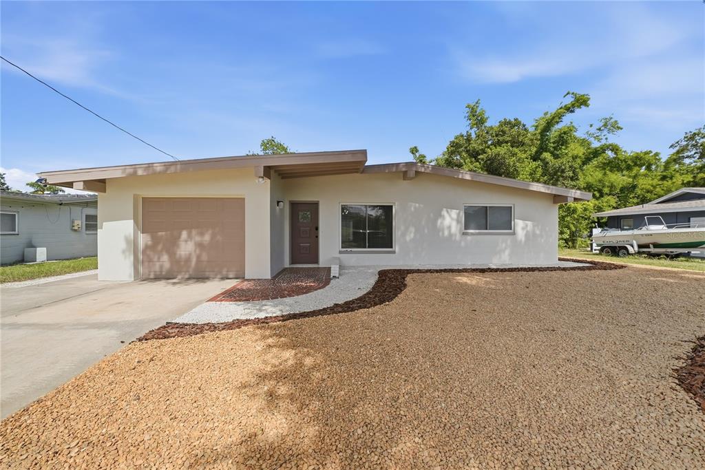 A single-story house with a beige exterior, a one-car garage, and a gravel front yard — 197 OVERBROOK DRIVE E, LARGO, FL